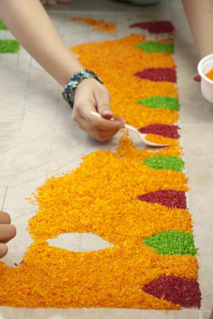 Person der laver rangoli kunstværk med orange ris og farvede blade